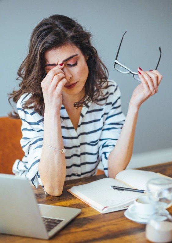 Woman at a desk with laptop holding the bridge of her nose and looking harassed